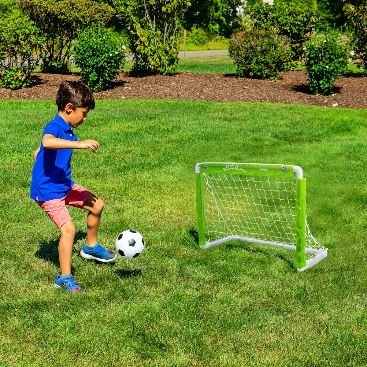 Child playing soccer with a goal in a grassy area